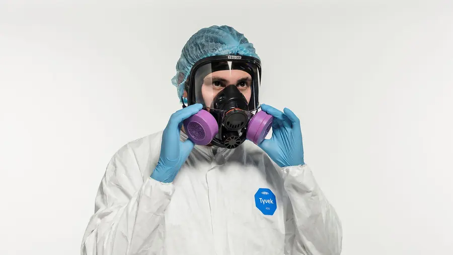 Technicien portant une combinaison de protection, un masque respiratoire à cartouches et des gants.